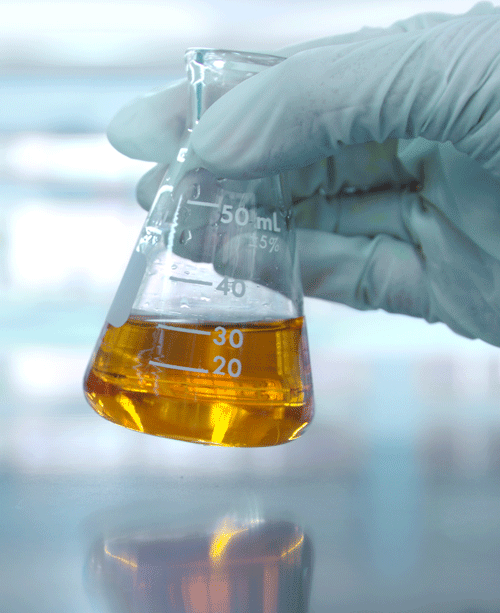 A person’s hand holding a chemical flask with an orange solution