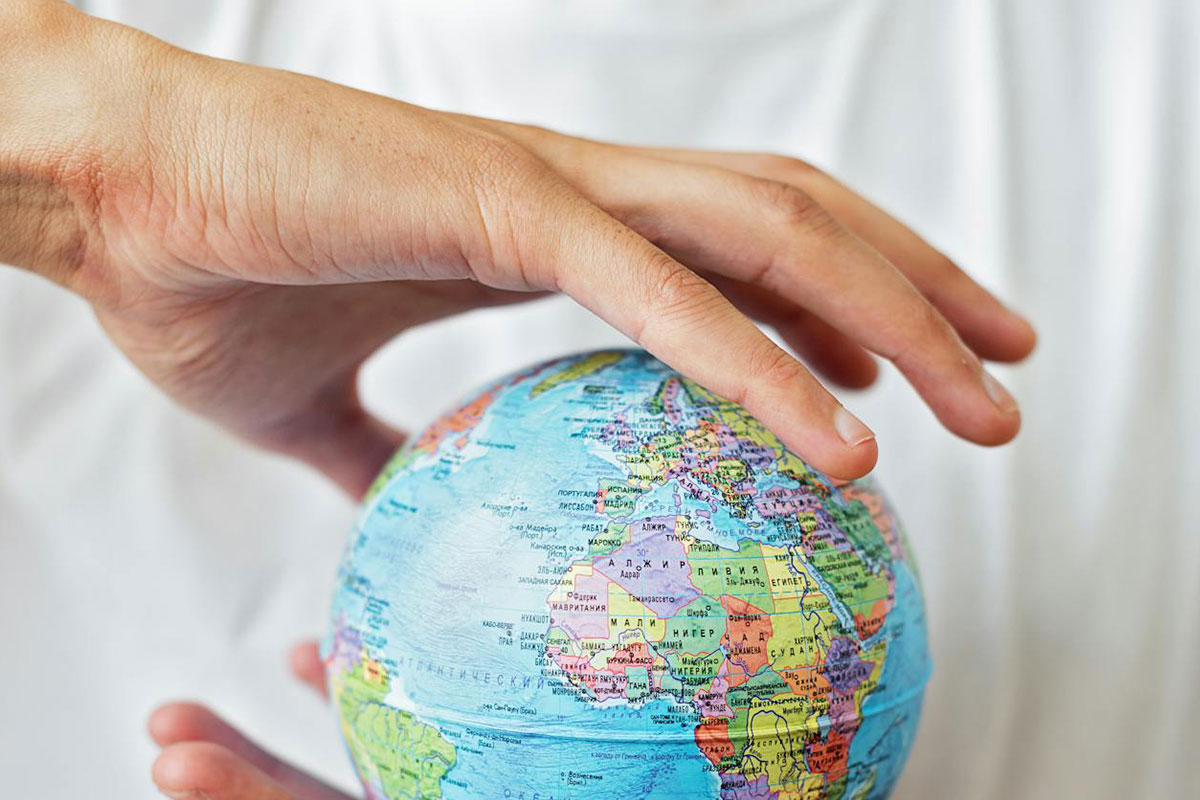 A person in a white t-shirt holds a small globe between their hands